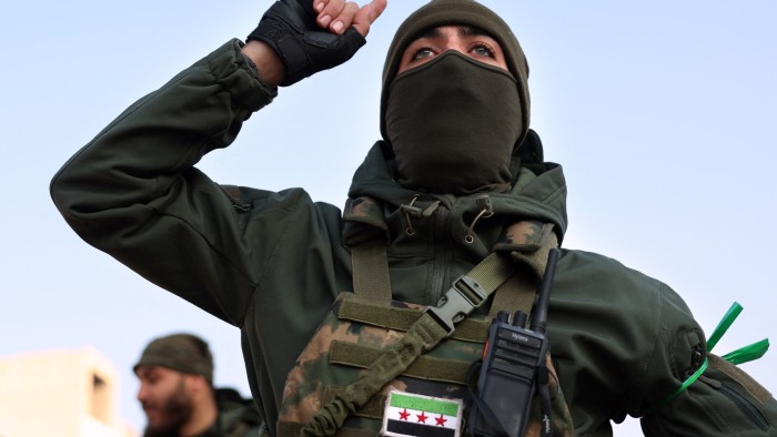 A rebel fighter wearing a balaclava raises his arm