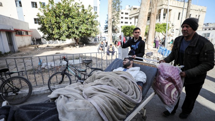 A man in a hospital bed is wheeled outside the hospital