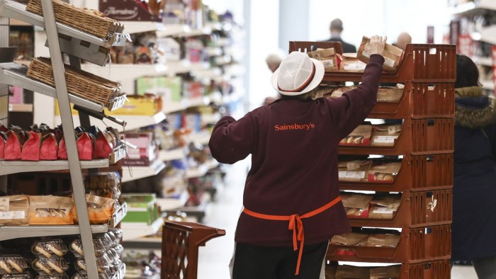 A Sainsbury's employee restocks shelves with bags of freshly made donuts in the baked goods aisle of a supermarket